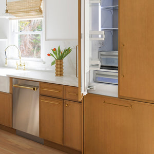 ZLINE Autograph Edition 24 in. Monument Series 3rd Rack Dishwasher with Auto Door Open Drying, 44dBa, Stainless Steel Panel with Polished Gold Handle (DWMTZ-304-24-G) in a kitchen with wooden cabinets, stainless steel appliances, and a vase with flowers on the counter.