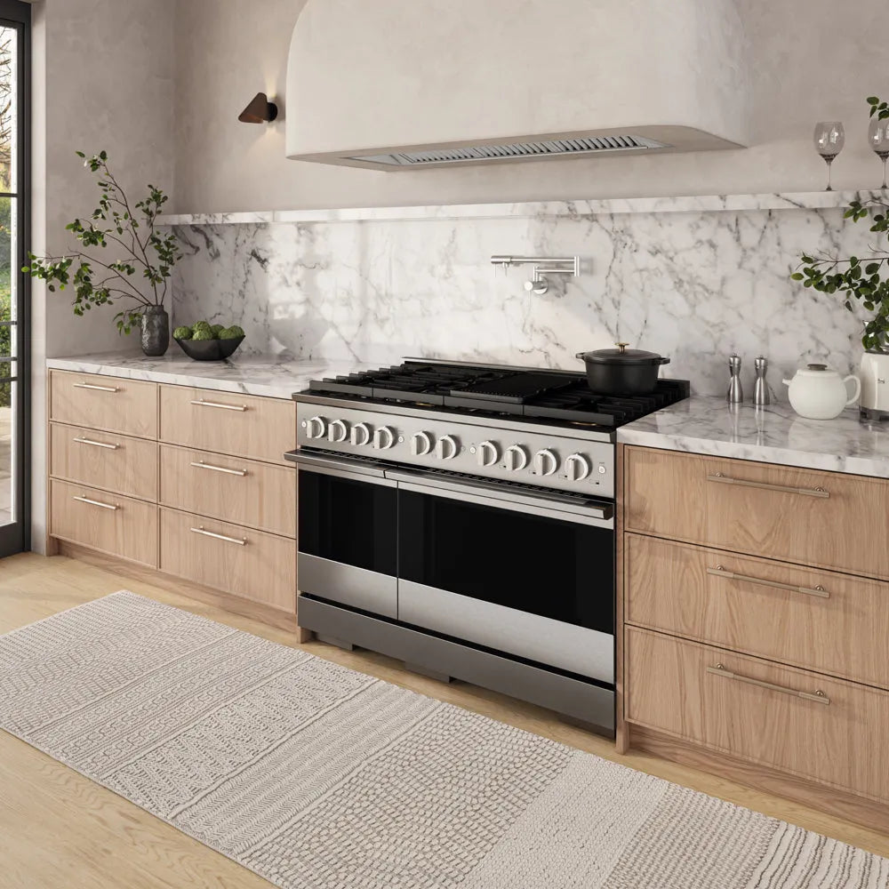 ZLINE 48 in. 6.7 cu. ft. Marino Double Oven Dual Fuel Range in Stainless Steel with 8 Brass Burners (MDR-BR-48) side, set in a modern kitchen with light wood cabinets, a white marble backsplash, and a textured beige rug.