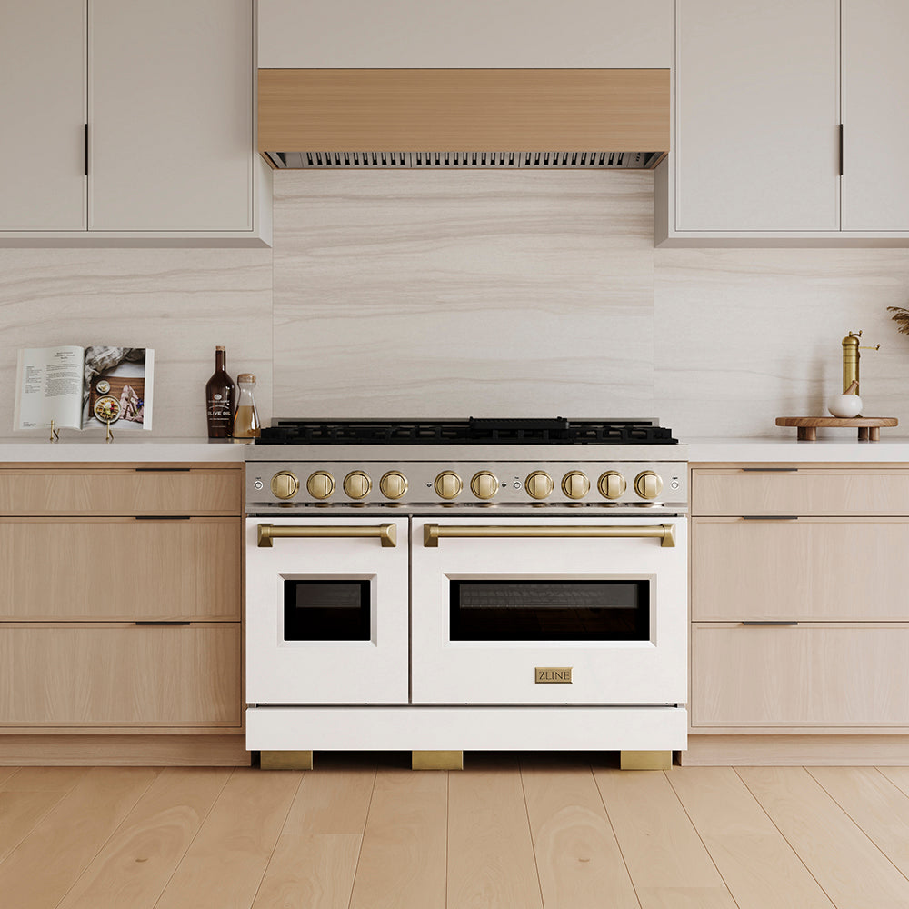 ZLINE Autograph Edition 48 in. 6.7 cu. ft. Classic Dual Fuel Range with 8 Burner DuoPro™ Cooktop and Dual Ovens with White Matte Doors and Champagne Bronze Accents (PCDRZ-WM-48-CB) in a custom kitchen with wooden cabinets and white walls, front.