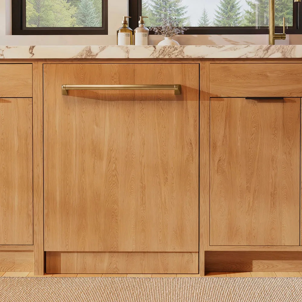 ZLINE Autograph Edition 24 in. Monument Series 3rd Rack Dishwasher with Auto Door Open Drying, 44dBa, Panel Ready with Champagne Bronze Handle (DWMTZ-24-CB) front, in a kitchen with wooden cabinets and a window view.