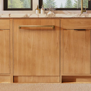 ZLINE Autograph Edition 24 in. Monument Series 3rd Rack Dishwasher with Auto Door Open Drying, 44dBa, Panel Ready with Champagne Bronze Handle (DWMTZ-24-CB) front, in a kitchen with wooden cabinets and a window view.