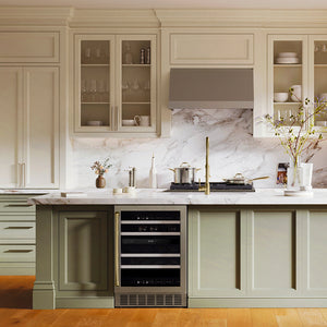 ZLINE Autograph Edition 24 in. Monument Dual Zone 44 Bottle Wine Cooler in Stainless Steel with Champagne Bronze Accents (RWVZ-UD-24-CB) in a kitchen with a marble backsplash, stainless steel appliances, and light wood cabinets.