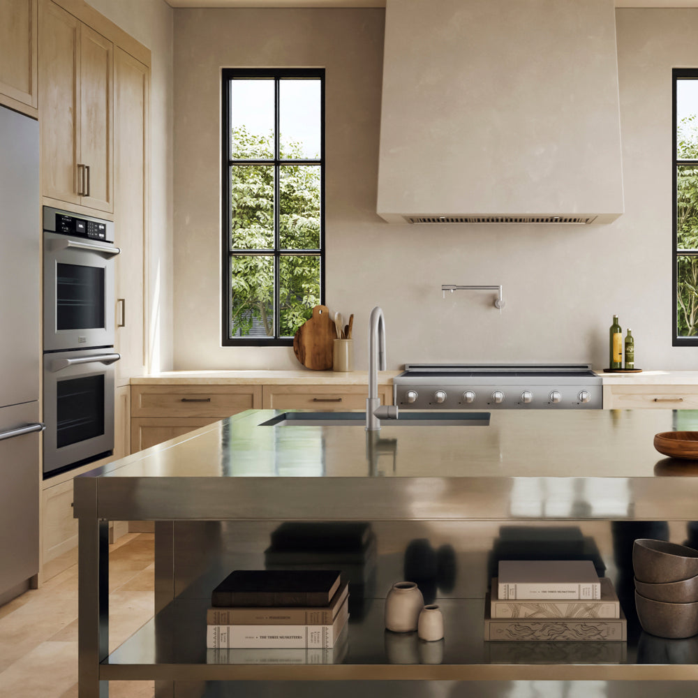 A ZLINE 48 in. Paramount Induction Rangetop with 7 Element Cooktop in Stainless Steel (SINRT48) in a modern kitchen with light wood cabinetry, stainless steel appliances, a large stainless steel island, a white range hood, and black-framed windows looking out to greenery.