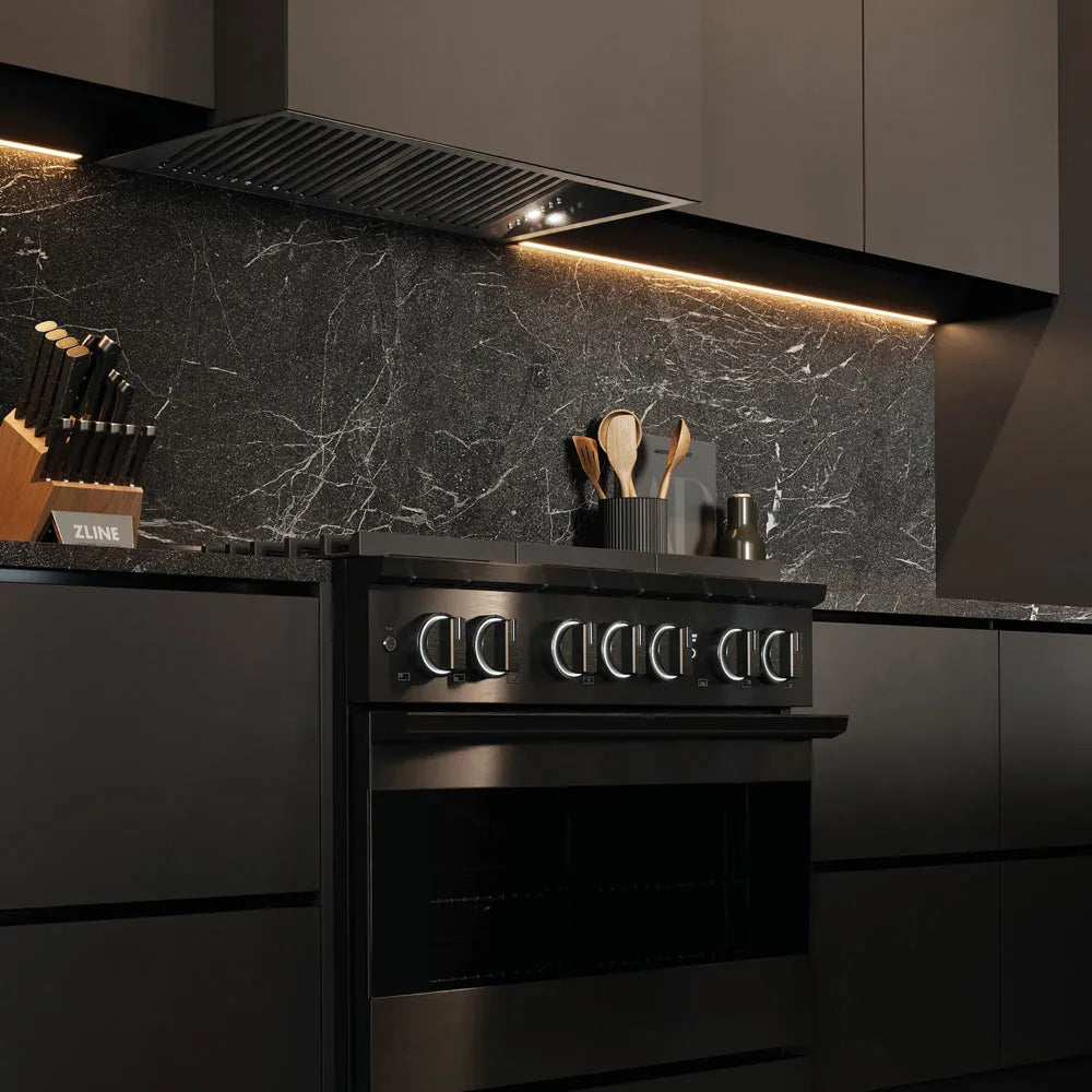 ZLINE 36 in. 5.2 cu. ft. Marino Dual Fuel Range with 6 Burner Gas Cooktop and Electric Convection Oven in Black Stainless Steel (MDRB-36) side, in a modern kitchen with a matching black range hood and a dark gray marble backsplash. Under-cabinet lighting is illuminated, and kitchen utensils are visible on the counter.