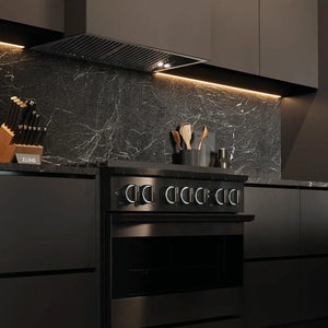 ZLINE 36 in. 5.2 cu. ft. Marino Dual Fuel Range with 6 Burner Gas Cooktop and Electric Convection Oven in Black Stainless Steel (MDRB-36) side, in a modern kitchen with a matching black range hood and a dark gray marble backsplash. Under-cabinet lighting is illuminated, and kitchen utensils are visible on the counter.