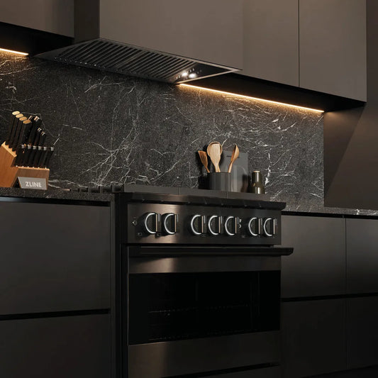 ZLINE 36 in. 5.2 cu. ft. Marino Dual Fuel Range with 6 Burner Gas Cooktop and Electric Convection Oven in Black Stainless Steel (MDRB-36) side, in a modern kitchen with a matching black range hood and a dark gray marble backsplash. Under-cabinet lighting is illuminated, and kitchen utensils are visible on the counter.