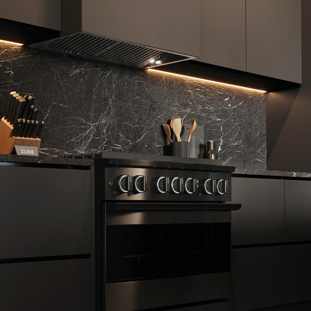 ZLINE 36 in. 5.2 cu. ft. Marino Gas Range with Convection Gas Oven in Black Stainless Steel with 6 Brass Burners (MGRB-BR-36) side, in a modern kitchen with a matching black range hood and a dark gray marble backsplash. Under-cabinet lighting is illuminated, and kitchen utensils are visible on the counter.