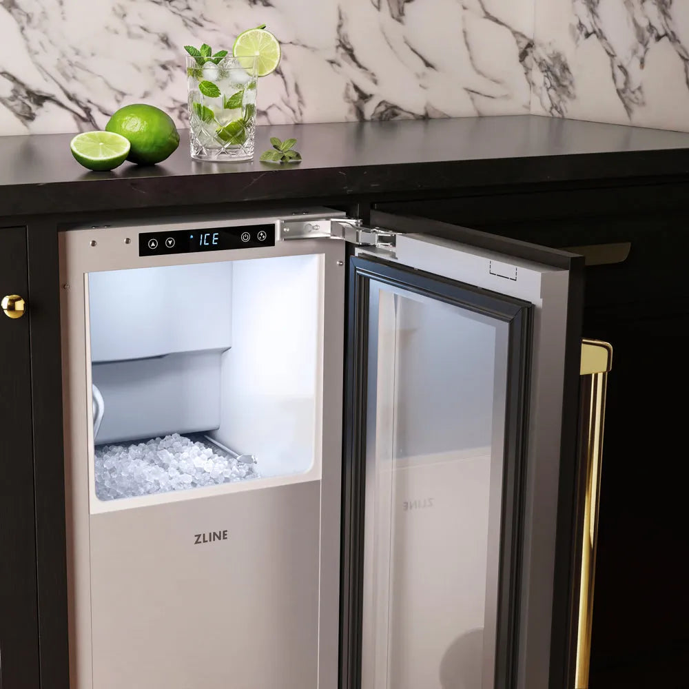 ZLINE Autograph Edition 15 in. Touchstone Nugget Ice Maker with Drain Pump and Panel-Ready Door with Polished Gold Handle (INGDPZ-15-G), shown open with ice inside installed in a cabinet beneath a black countertop with a marble backsplash.