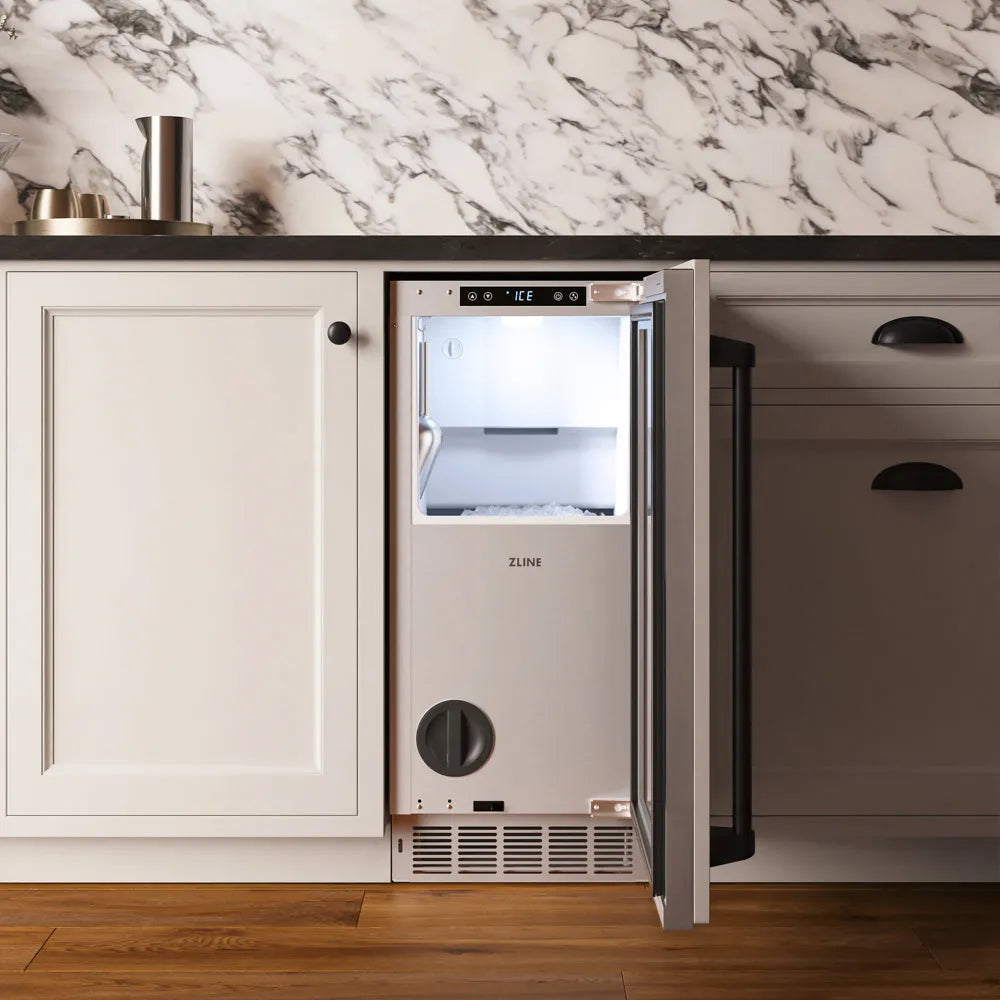 ZLINE Autograph Edition 15 in. Touchstone Nugget Ice Maker with Drain Pump and Panel-Ready Door with Matte Black Handle (INGDPZ-15-MB) with its door open, set into a kitchen cabinet with a dark countertop and marble backsplash.