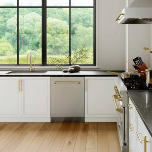 Modern kitchen with white cabinets, ZLINE Autograph Edition 24 in. Tallac Series 3rd Rack Top Control Built-In Tall Tub Dishwasher in Stainless Steel with Champagne Bronze Handle, 51dBa (DWVZ-304-24-CB), and a view of greenery outside.