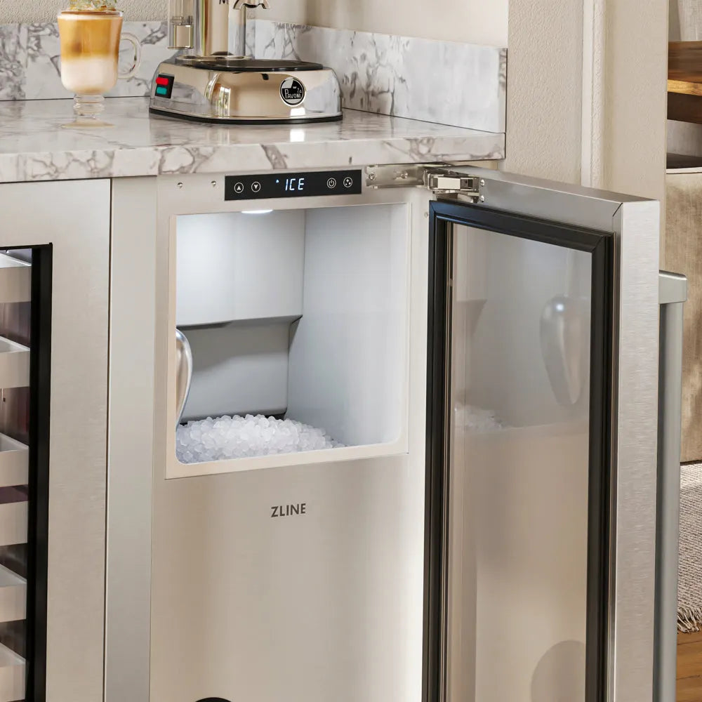 ZLINE 15 in. Touchstone Nugget Ice Maker with Drain Pump and Solid Stainless Steel Door (INGD-ST-15) with its door open, showing a digital display and a compartment filled with ice, installed under a marble countertop in a kitchen setting.