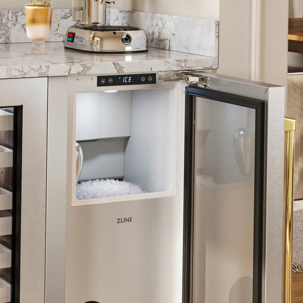ZLINE Autograph Edition 15 in. Touchstone Nugget Ice Maker with Drain Pump and Solid Stainless Steel Door with Polished Gold Handle (INGDZ-ST-15-G) with its door open, showing a digital display and a compartment filled with ice, installed under a marble countertop in a kitchen setting.