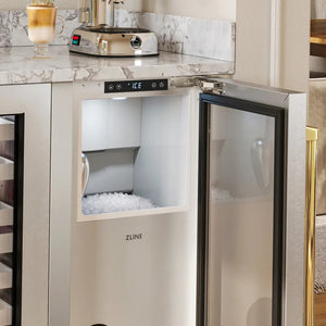 ZLINE Autograph Edition 15 in. Touchstone Nugget Ice Maker with Drain Pump and Solid Stainless Steel Door with Polished Gold Handle (INGDZ-ST-15-G) with its door open, showing a digital display and a compartment filled with ice, installed under a marble countertop in a kitchen setting.