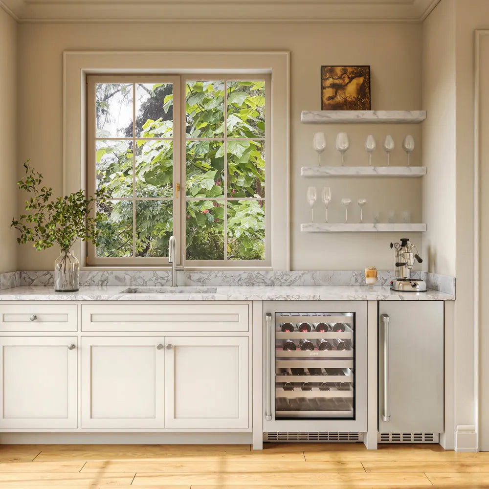 A modern kitchen island featuring white shaker cabinets, a gray and white marble countertop, a built-in ZLINE 15 in. Touchstone Nugget Ice Maker with Drain Pump and Solid Stainless Steel Door (INGD-ST-15), set against beige walls with a window showing green foliage outside.