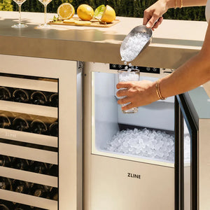 An outdoor beverage station with a ZLINE wine cooler on the left and a ZLINE 15 in. Touchstone Nugget Ice Maker with Drain Pump and Solid Stainless Steel Door (INGD-ST-15) on the right, shown in use with a person pouring ice from a metal scoop into a glass.