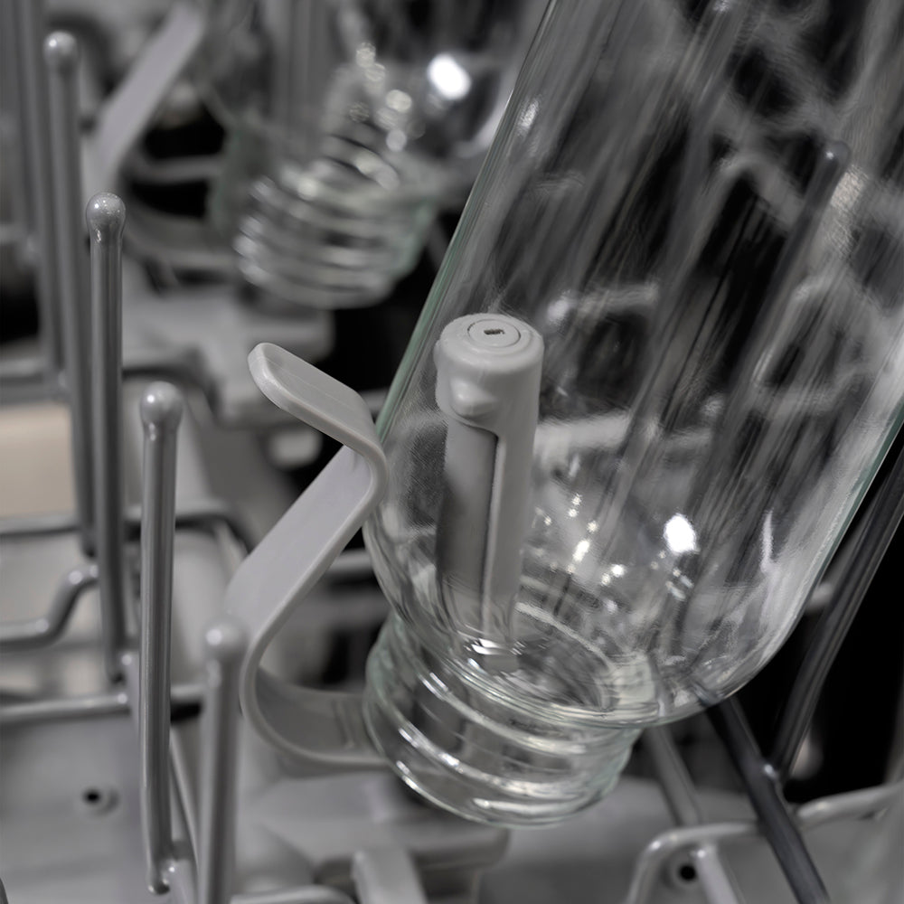 Close-up of a clear glass bottle on a bottle jet inside a ZLINE Autograph Edition 24 in. Monument Series 3rd Rack Dishwasher with Auto Door Open Drying, 44dBa, Stainless Steel Panel with Polished Gold Handle (DWMTZ-304-24-G).