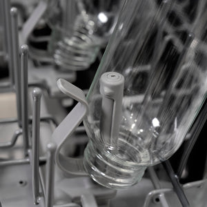 Close-up of a clear glass bottle on a bottle jet inside a ZLINE Autograph Edition 24 in. Monument Series 3rd Rack Dishwasher with Auto Door Open Drying, 44dBa, Stainless Steel Panel with Polished Gold Handle (DWMTZ-304-24-G).