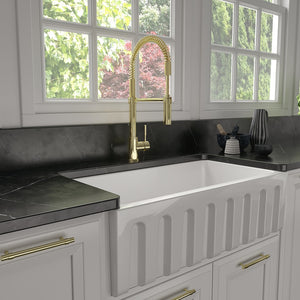 ZLINE Sierra Pull Down Spring Single Handle Kitchen Faucet in Polished Gold (SRA-KF-PG) in a kitchen with a white farmhouse sink, black countertop, and gold accents.