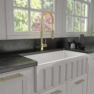 ZLINE Sierra Pull Down Spring Single Handle Kitchen Faucet in Polished Gold (SRA-KF-PG) in a kitchen with a white farmhouse sink, black countertop, and gold accents.