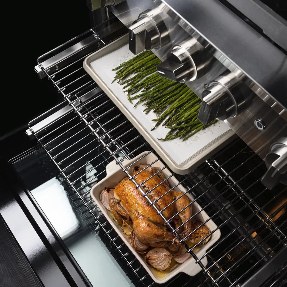 ZLINE 36 in. 5.2 cu. ft. Marino Gas Range with Convection Gas Oven in Stainless Steel with 6 Brass Burners (MGR-BR-36) close-up, oven racks, one holding a tray of green asparagus on a white liner and the other holding a roasted chicken in a white ceramic dish, shown from a high-angle view.