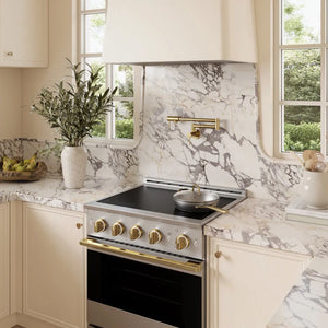 A modern kitchen scene featuring a ZLINE Autograph Edition 30 in. 4.2 cu. ft. Marino Induction Range with 4 Element Cooktop and Electric Convection Oven in Stainless Steel with Polished Gold Accents (MINRZ-30-G), set into cream-colored cabinets with a matching marble backsplash and countertop.