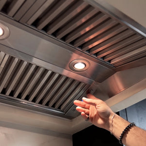ZLINE 46 in. Ducted Wall Mount Range Hood Insert in Outdoor Approved Stainless Steel (721-304-46), person reaching towards the cooktop lights and fan control buttons.