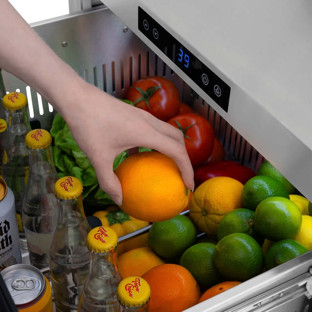 Hand reaching into a ZLINE 24 in. Touchstone 168 Can Outdoor-Rated Dual Refrigerator Drawer with Hand Hammered Copper Doors (RDSO-HH-24)  filled with fruits and drinks, with a digital display showing 39 degrees.