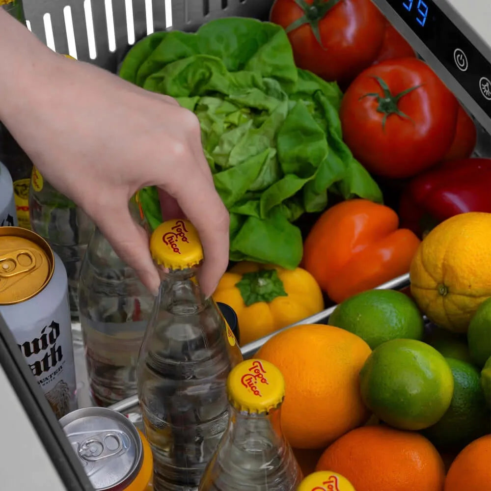 Hand reaching for a bottle amidst fruits and vegetables in a ZLINE 24 in. Touchstone 168 Can Outdoor-Rated Dual Refrigerator Drawer with Hand Hammered Copper Doors (RDSO-HH-24).