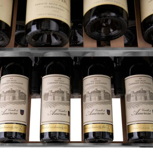 ZLINE Autograph Edition 24 in. Monument Dual Zone 44-Bottle Wine Cooler in Stainless Steel with Matte Black Accents (RWVZ-UD-24-MB) close-up, four bottles of Cabernet Sauvignon on an extended wood shelf from above.