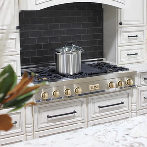 Stainless steel pot on a ZLINE Autograph Edition 48 in. Legacy Gas Rangetop with 7 Burners and Porcelain Cooktop in Stainless Steel with Polished Gold Accents (RTZ-48-G) with white cabinets and black backsplash.