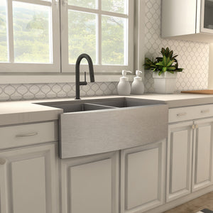 ZLINE Voltaire Pull Down Single Handle Kitchen Faucet in Matte Black (VLT-KF-MB) above a farmhouse sink next to light-colored cabinets.